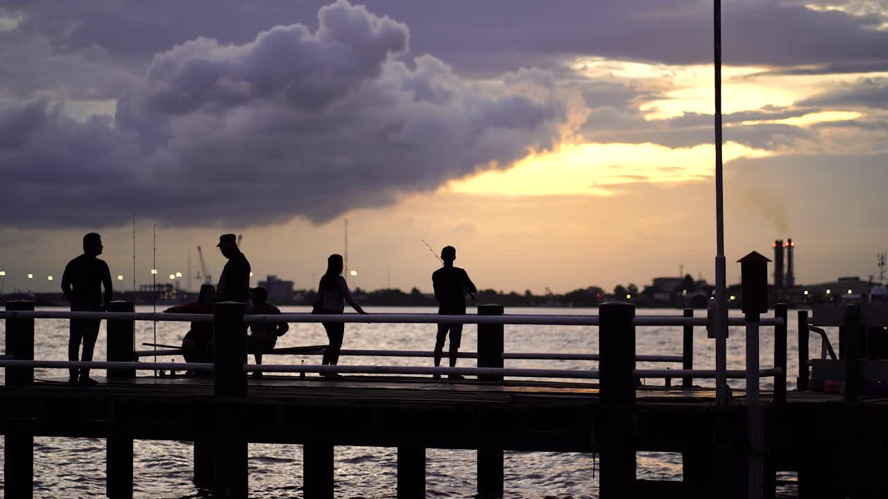 Silhouettes of People Fishing at Sunset on a Pier