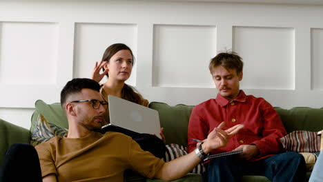 three members of a study group sitting on sofa and floor discussing about a project