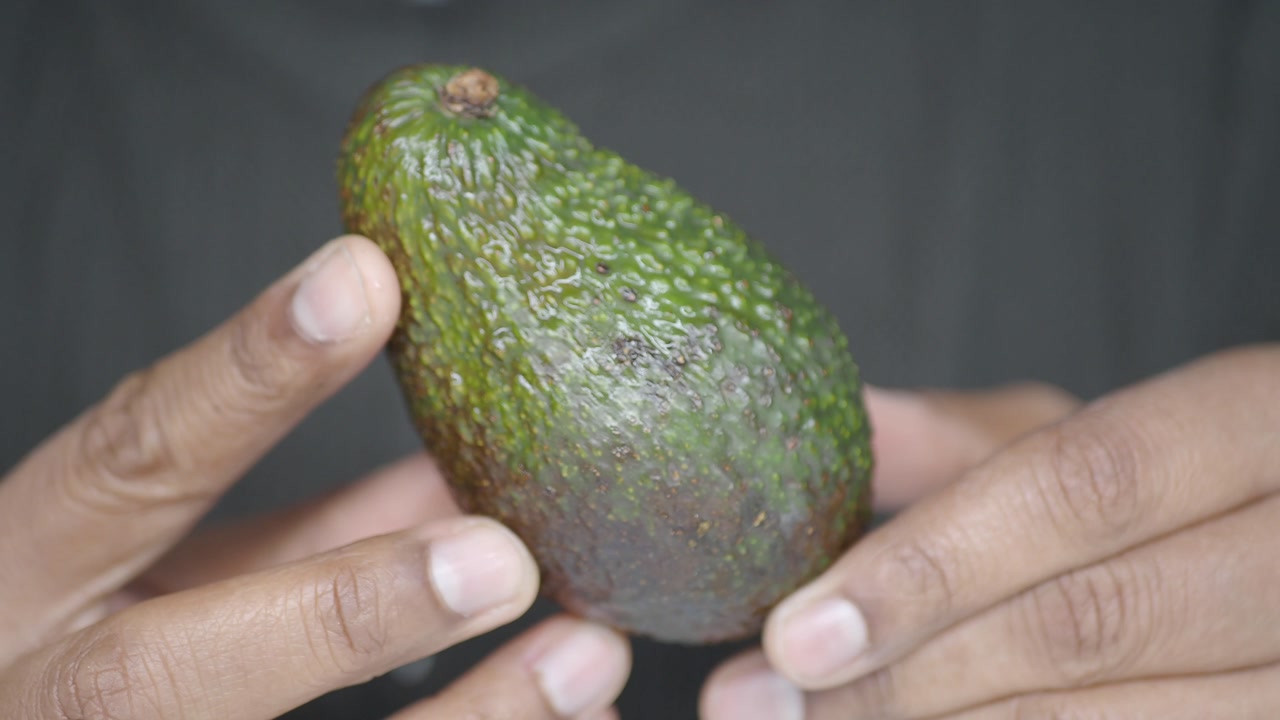 Close-Up of Hands Holding and Examining a Fresh Green Avocado