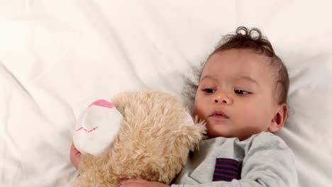 un bebé lindo en una cama con un oso de peluche