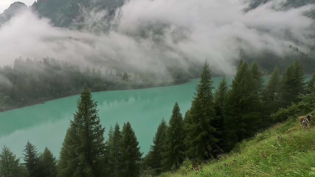 Clouds Drift Above the Emerald Waters of Lago Alpe del Cavalli Surrounded by Pine Trees and Alpine Slopes in Piedmont, Italy