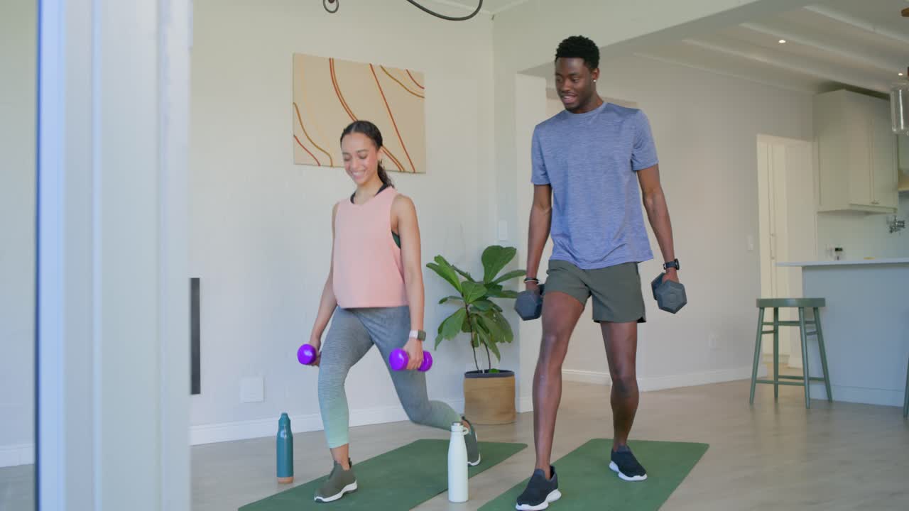 Male and female in workout clothes holding dumbbells on mats at home, performing lunges for form