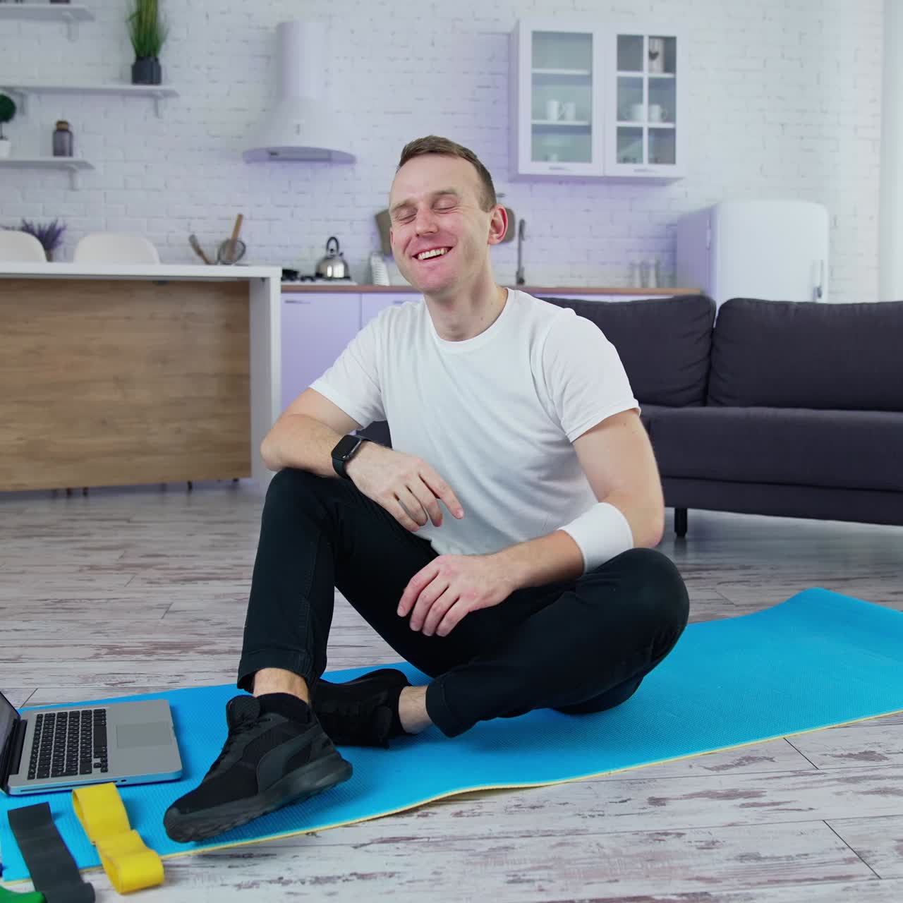 Handsome young sportsman doing exercises on quarantine. Lively athletic active man using his laptop and drinking water while training indoors