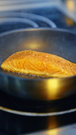 piece of salmon sprinkled with spices is fried on the frying pan. metal tongs turn the fish on the other side. close up. vertical video.