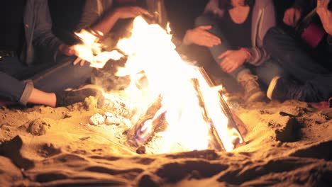 closeup view of the bonfire late at night. young people sitting by the fire in the evening, playing guitar. cheerful friends singing songs, talking and having fun together