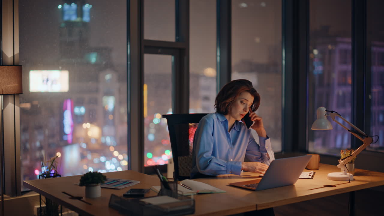 Worried businesswoman calling dark office with night city view. Concerned woman