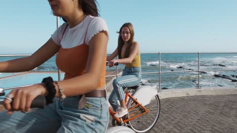 side view of a caucasian and a mixed race girl riding a bike seaside