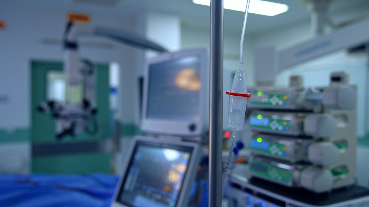 Un fleboclisi che gocciola nella sala operatoria. Primo piano. Diverse moderne attrezzature mediche sfocate sullo sfondo.