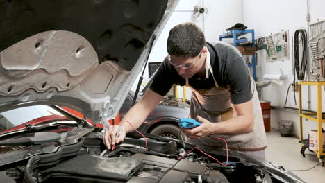 Mechanic-checking-a-car-with-a-multimeter-in-garage-with-tools-on-the-wall