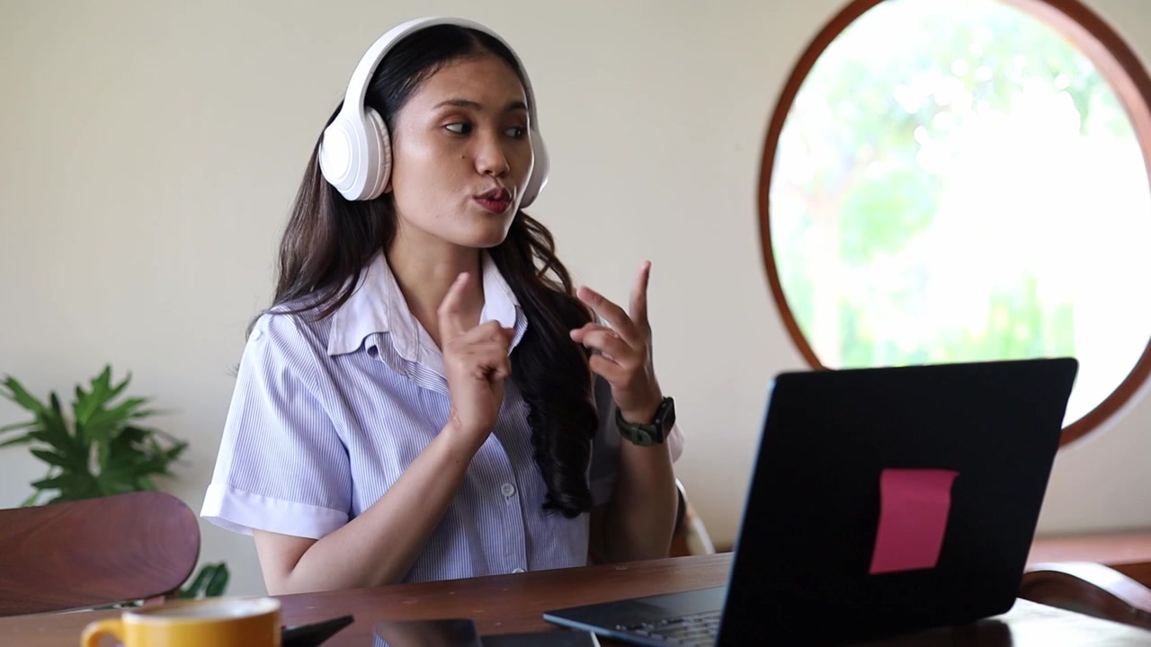 Empresária asiática com fones de ouvido em videochamada, trabalhando em laptop em cafeteria, freelancer remoto em reunião online, apresentação, conversando