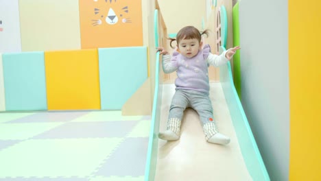 two-year-old baby girl sliding from kid's slider at indoor playground room