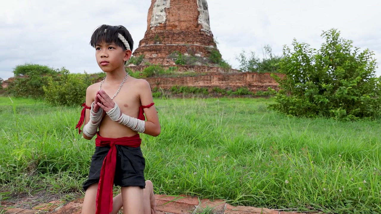Cậu bé châu Á trong trang phục võ thuật truyền thống thực hiện nghi lễ cầu nguyện trước những ngôi chùa đá cổ kính.