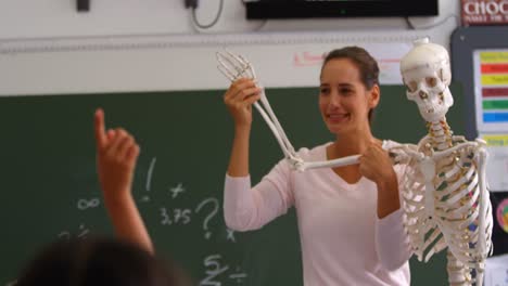 Front-view-of-Caucasian-female-teacher-explaining-human-skeleton-model-in-classroom-4k
