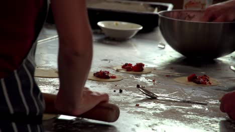 cooks are busily preparing pastry snacks, one rolling out the dough and others adding mix to the dough cutouts