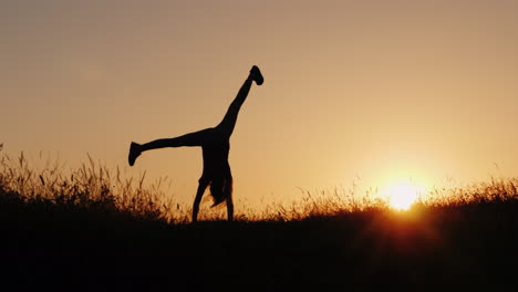 Silhouette-Eines-Kleinen-Mädchens,-Das-Ein-Akrobatisches-Rad-In-Einer-Wunderschönen-Sonnenuntergangskulisse-Macht