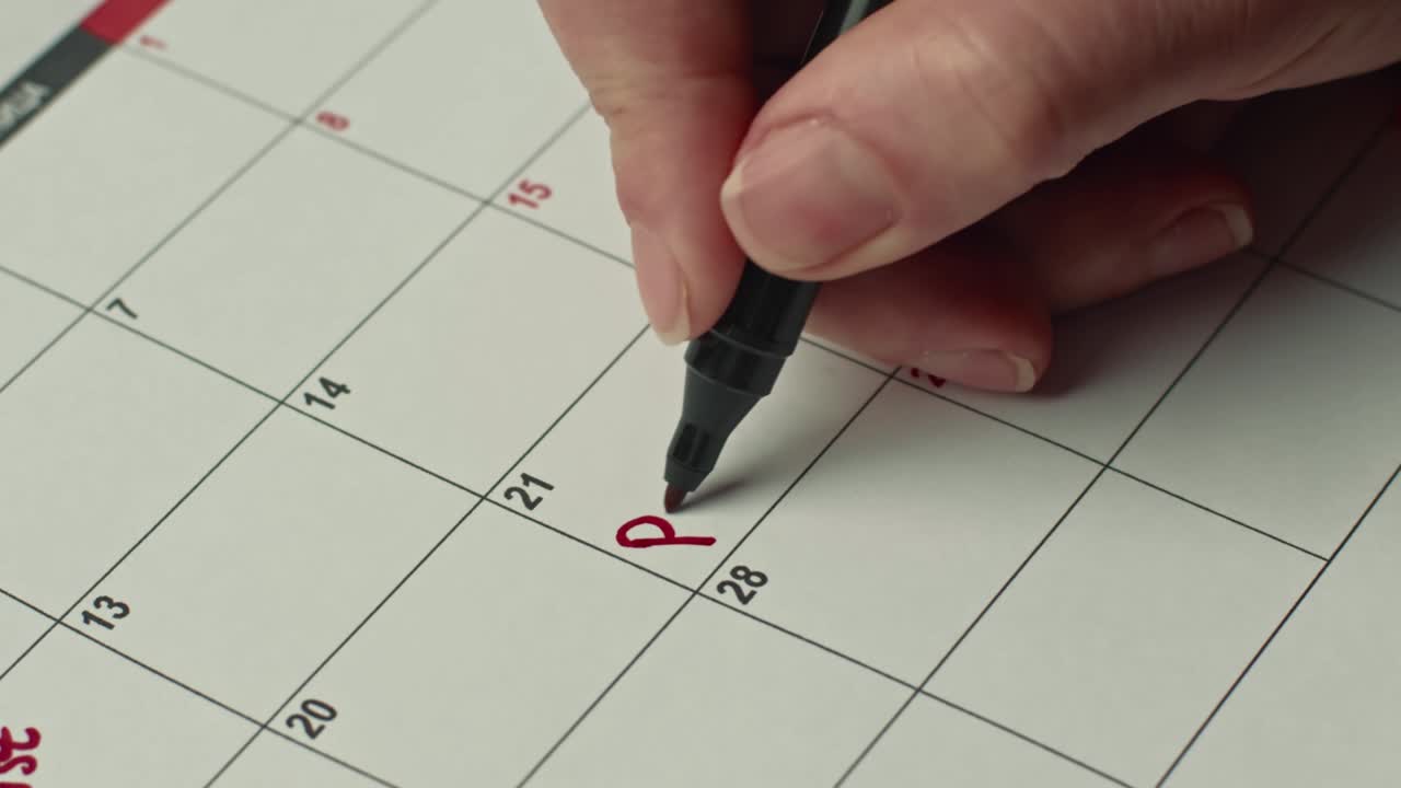Close up of female hand marking the day in calendar by writing PARTY as a reminder using a red pen