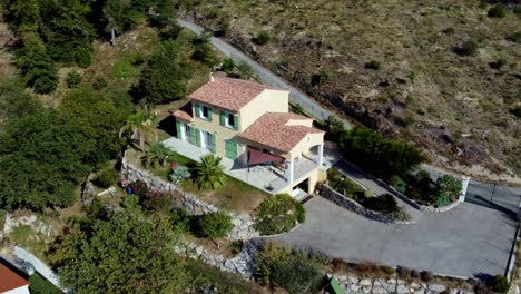 Volar-Lejos-De-Una-Casa-En-Una-Colina,-Al-Lado-De-Una-Zona-Residencial,-En-Carros,-Al-Sur-De-Francia,-Con-El-Pueblo-De-Carros-Y-La-Montaña-Al-Fondo