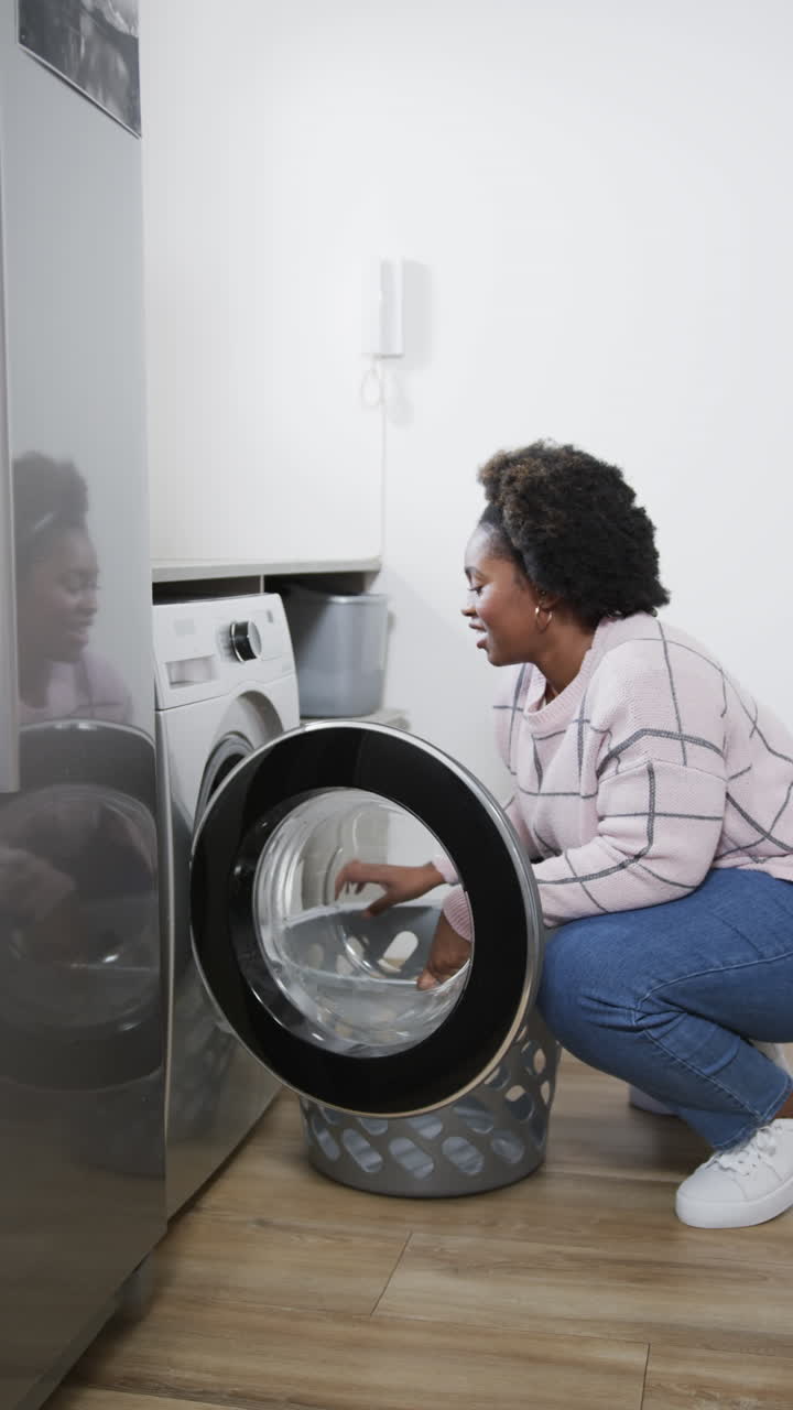 Vertical video of african american woman using washing machine and doing laundry at home