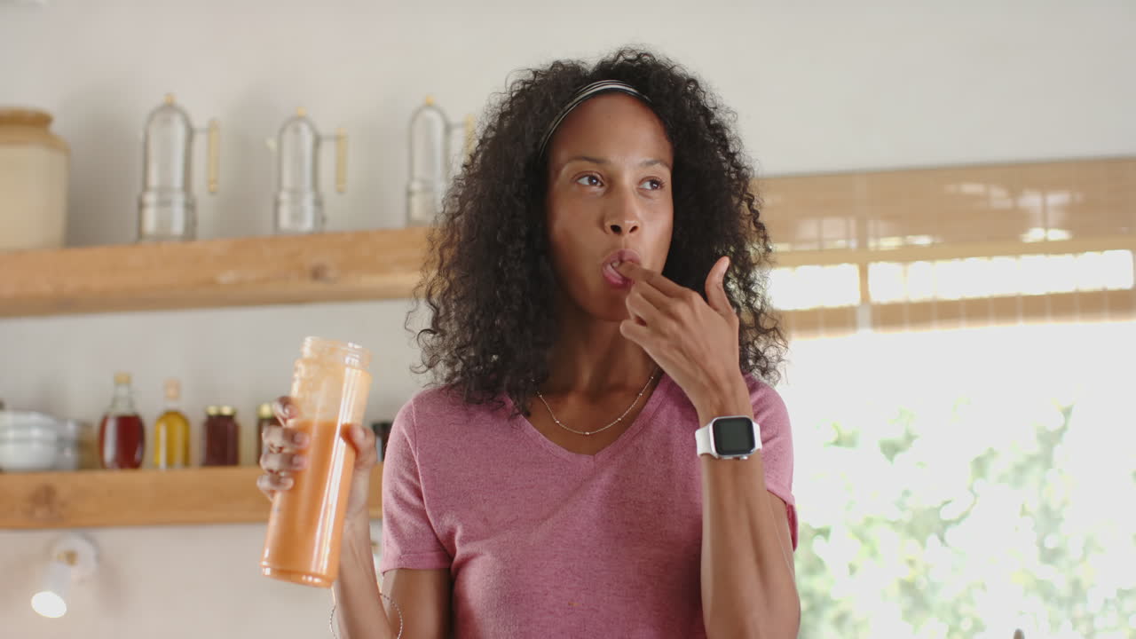 Smiling woman in kitchen pouring fresh juice into glass, enjoying morning routine, at home
