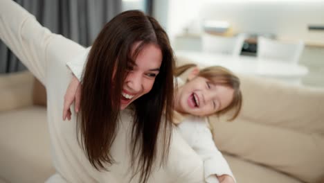 cheerful mother carrying small child girl on back bonding pretending flying having fun together