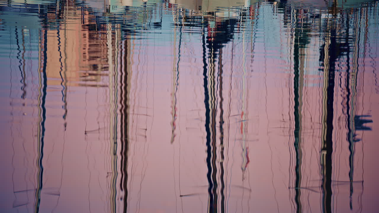 Close up of rippling water reflecting sailboat masts and harbor structures, forming abstract vertical patterns