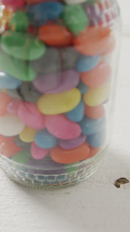 video of multi coloured jelly sweets in jar over white rustic background