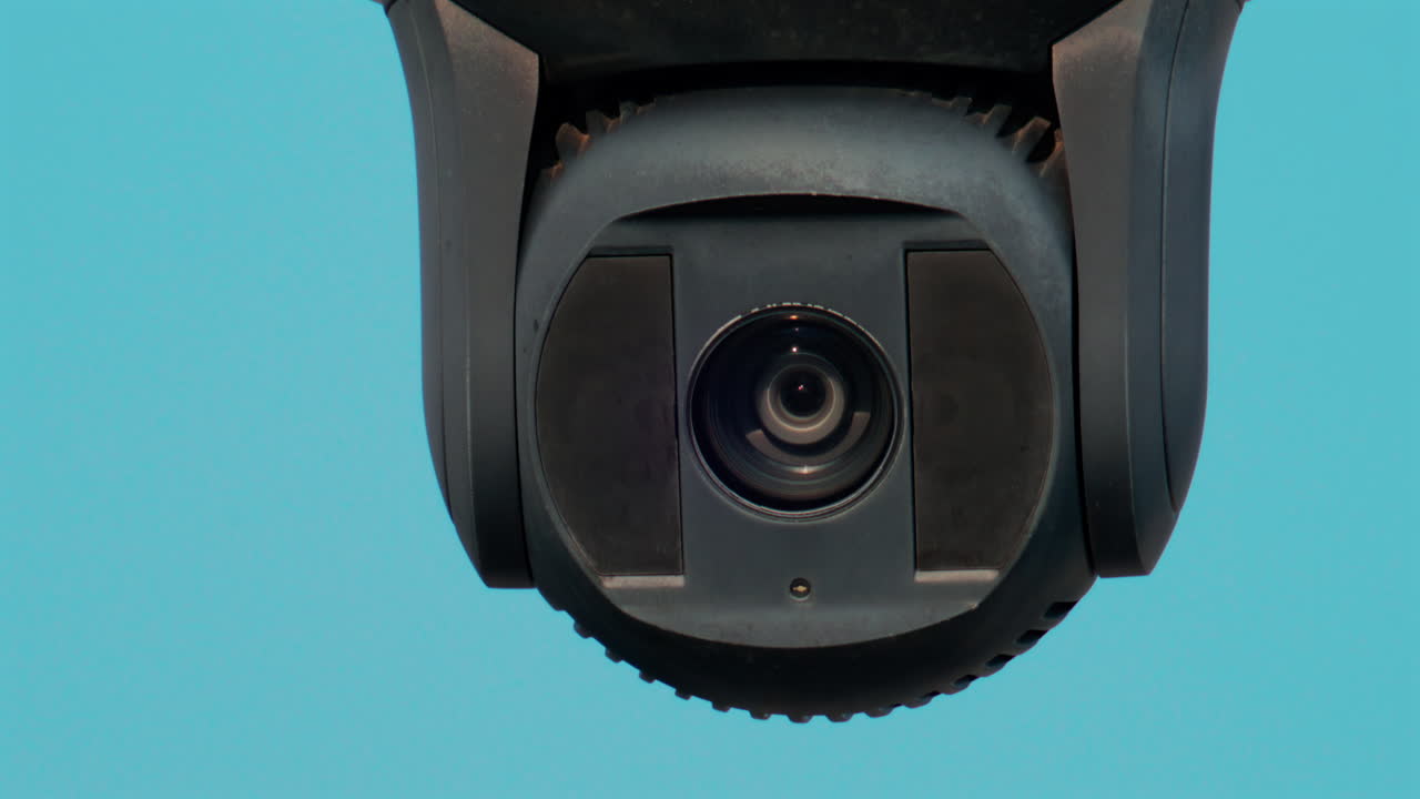 A close up of a modern black surveillance camera turning against a bright sky background