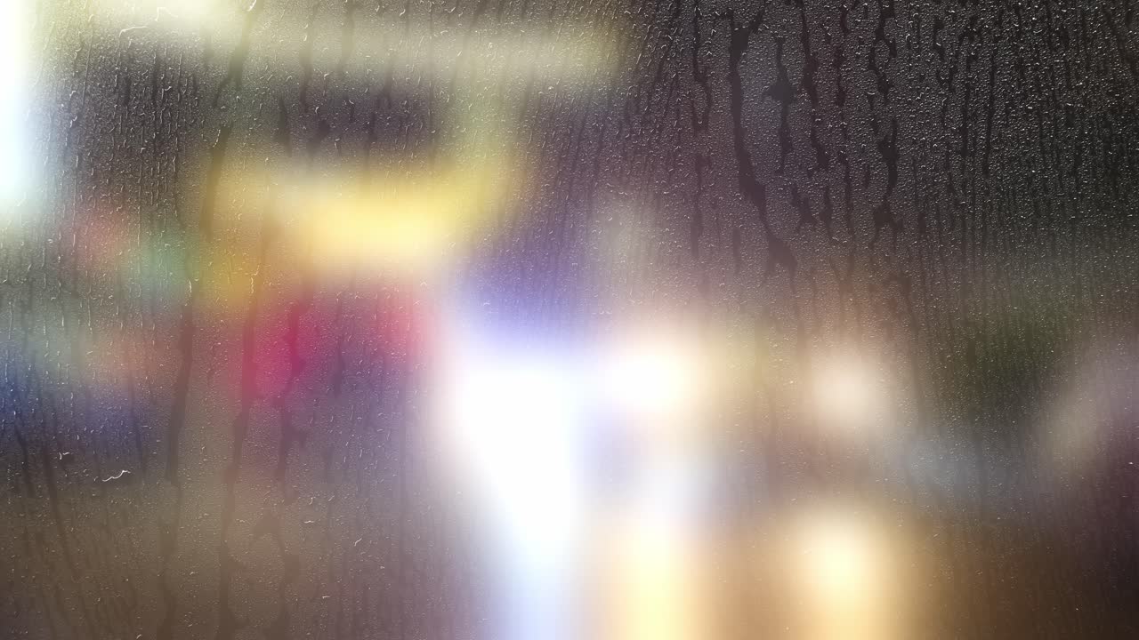 An abstract view of blurred city lights and movement seen through a window covered in condensation and water streaks. Creates a moody, atmospheric, and introspective feeling for various projects