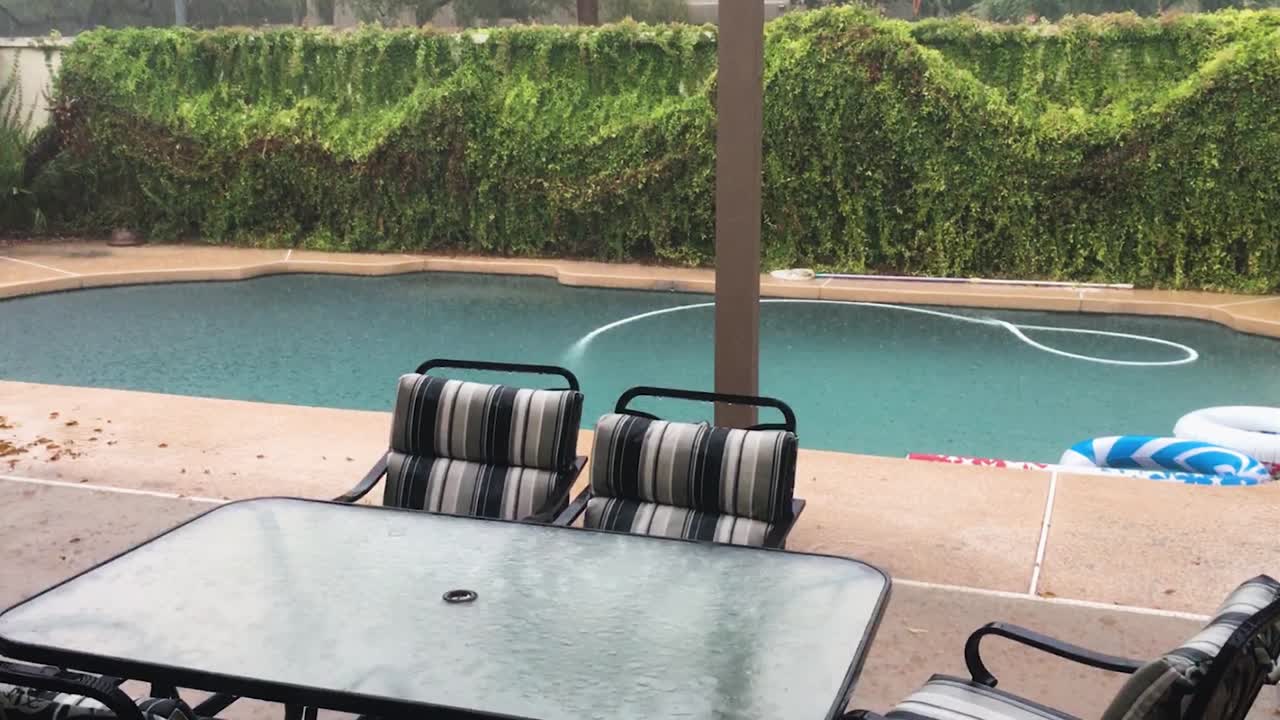 la lluvia torrencial rebota en el agua de la piscina y en la mesa de vidrio de una mesa junto a la piscina, scottsdale, arizona