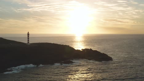 Panorama-drone-shot-of-a-lighthouse-at-golden-hour-with-ocean-and-sun