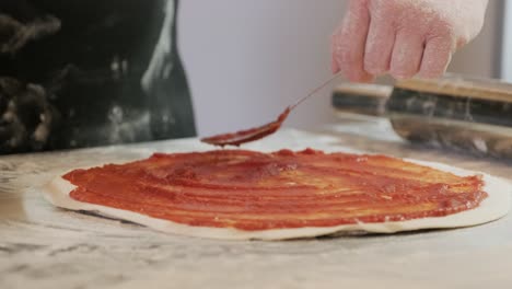 chef extendiendo salsa de tomate en la masa de pizza con un cucharón de metal en un restaurante de pizza