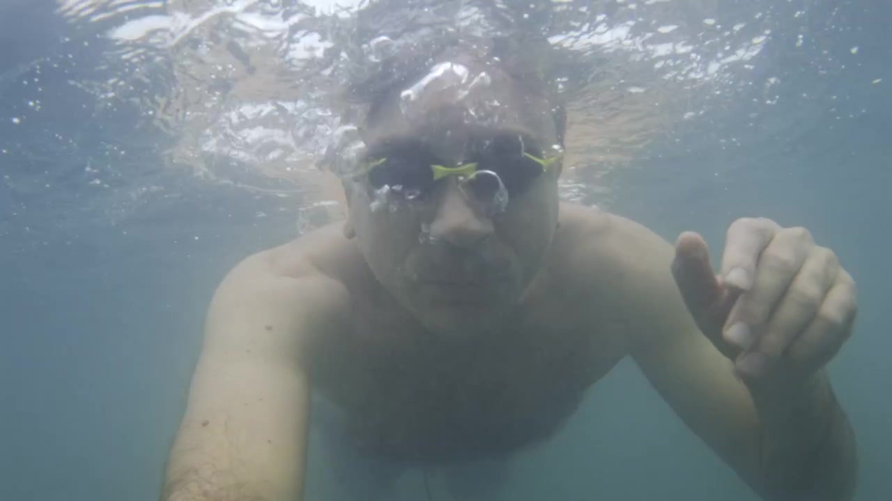 Uomo con occhialini gialli che crea bolle mentre nuota sott'acqua, mostrando un'attività acquatica rinfrescante.
