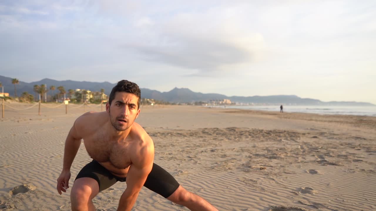 hombre hispano sin camisa entrenando con pesas rusas en la playa al amanecer