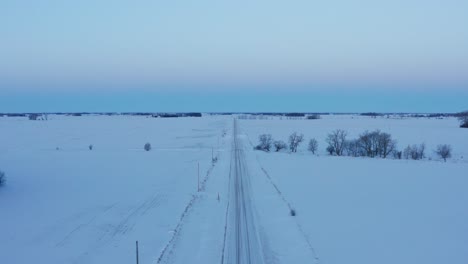 Aerial,-snow-covered-straight-road-in-rural-countryside,-vast-snow-field,-pastel-colors