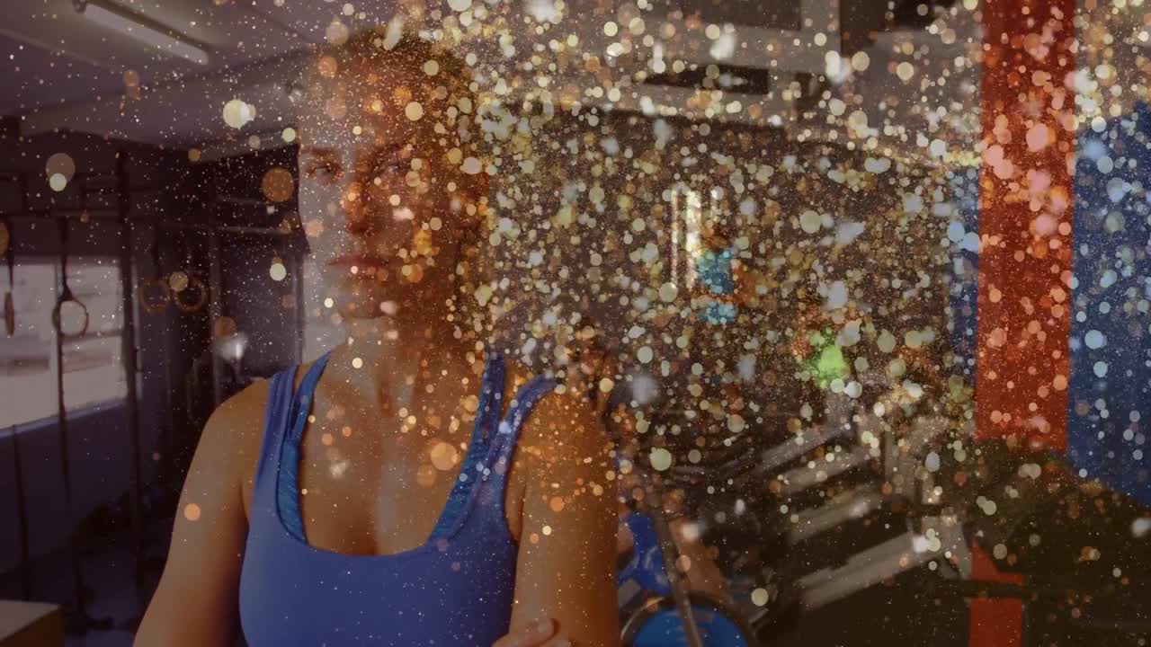 Kvindelig træner overvåger formen med armene krydset i fitnesscenter, i baggrunden cykler folk og der er glimt omkring træneren