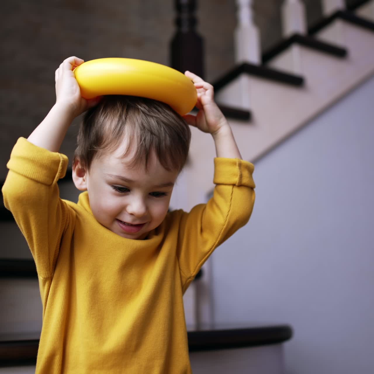 Smiling cute baby boy holding a ring from pyramid on the head. Happy child playing at home