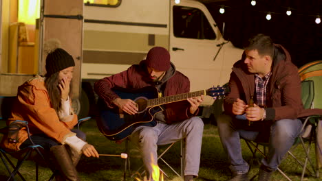 Niña-Sosteniendo-Malvavisco-Y-Uno-De-Sus-Amigos-Canta-En-Una-Guitarra