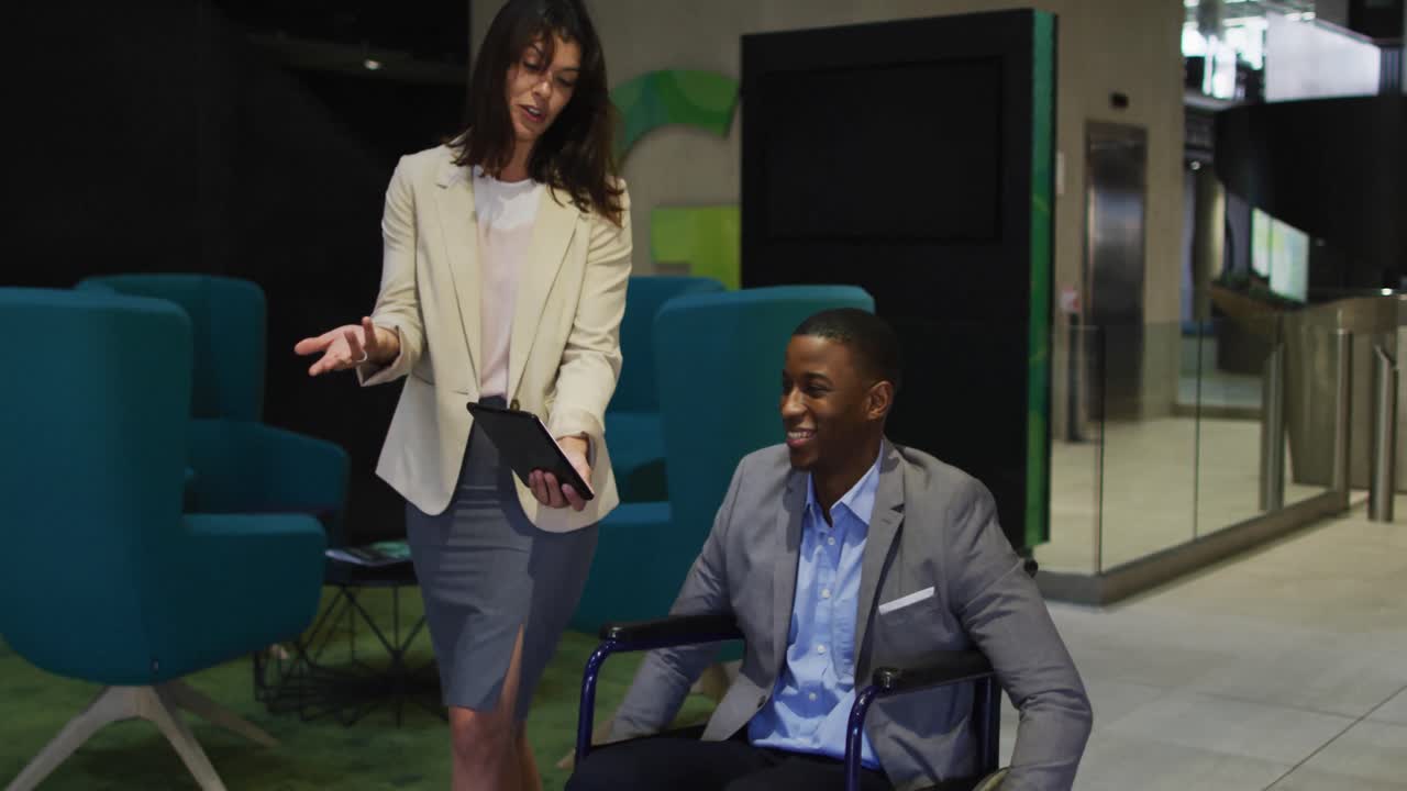 Femme d'affaires caucasienne et homme d'affaires afro-américain handicapé en fauteuil roulant utilisant une tablette