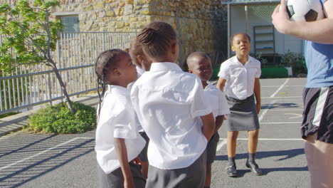 young kids in a school playground with teacher holding ball