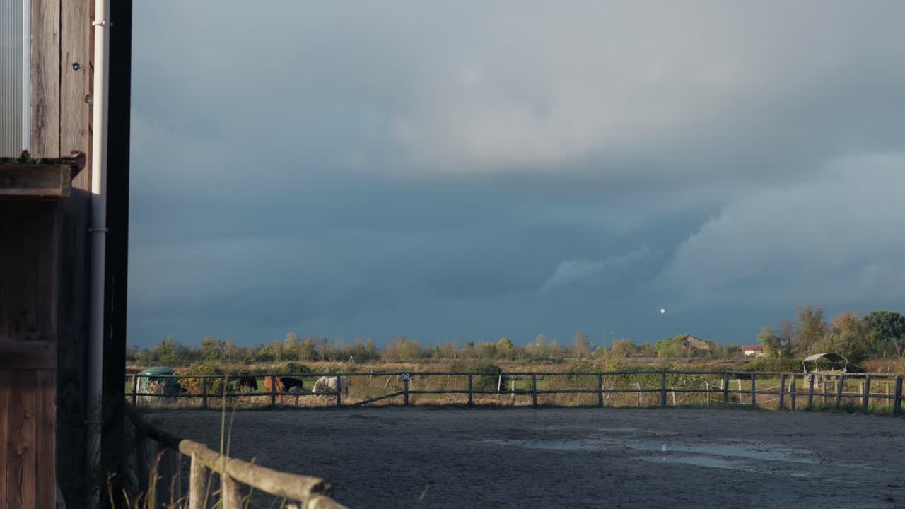 Hestefold og landligt landskab under mørke stormskyer efter regn. Stille landlig scene med hegn, marker og dramatisk himmel, der skaber en stemningsfuld naturlig atmosfære.