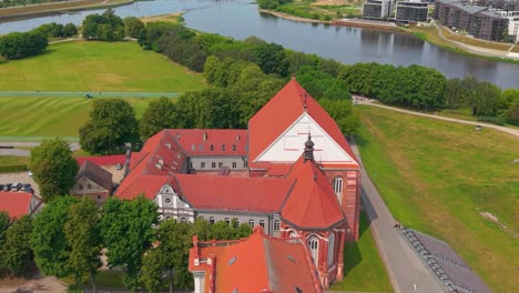 aerial view of a historic red-roofed church of st. george the martyr near a river and green park in kaunas, lithuania, showcasing european architecture and landscape