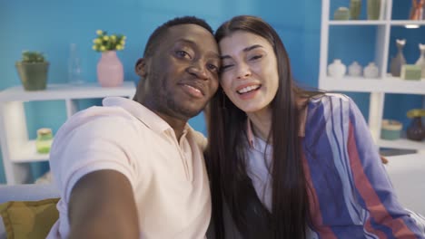 happy and funny african young man and his caucasian girlfriend taking selfie photo at home.