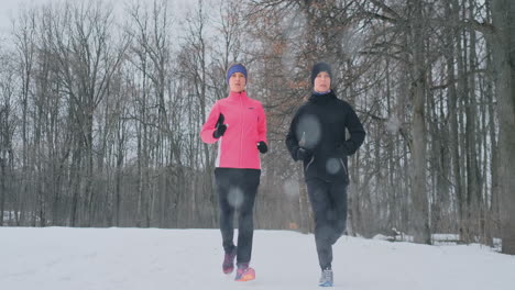 positive beautiful young healthy couple running with sportswear through the forest in the winter morning