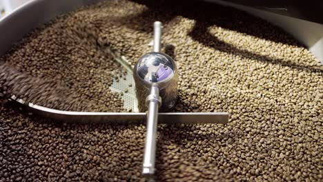 Wide-slow-motion-view-of-coffee-beans-tumbled-through-drum-machine-roasting