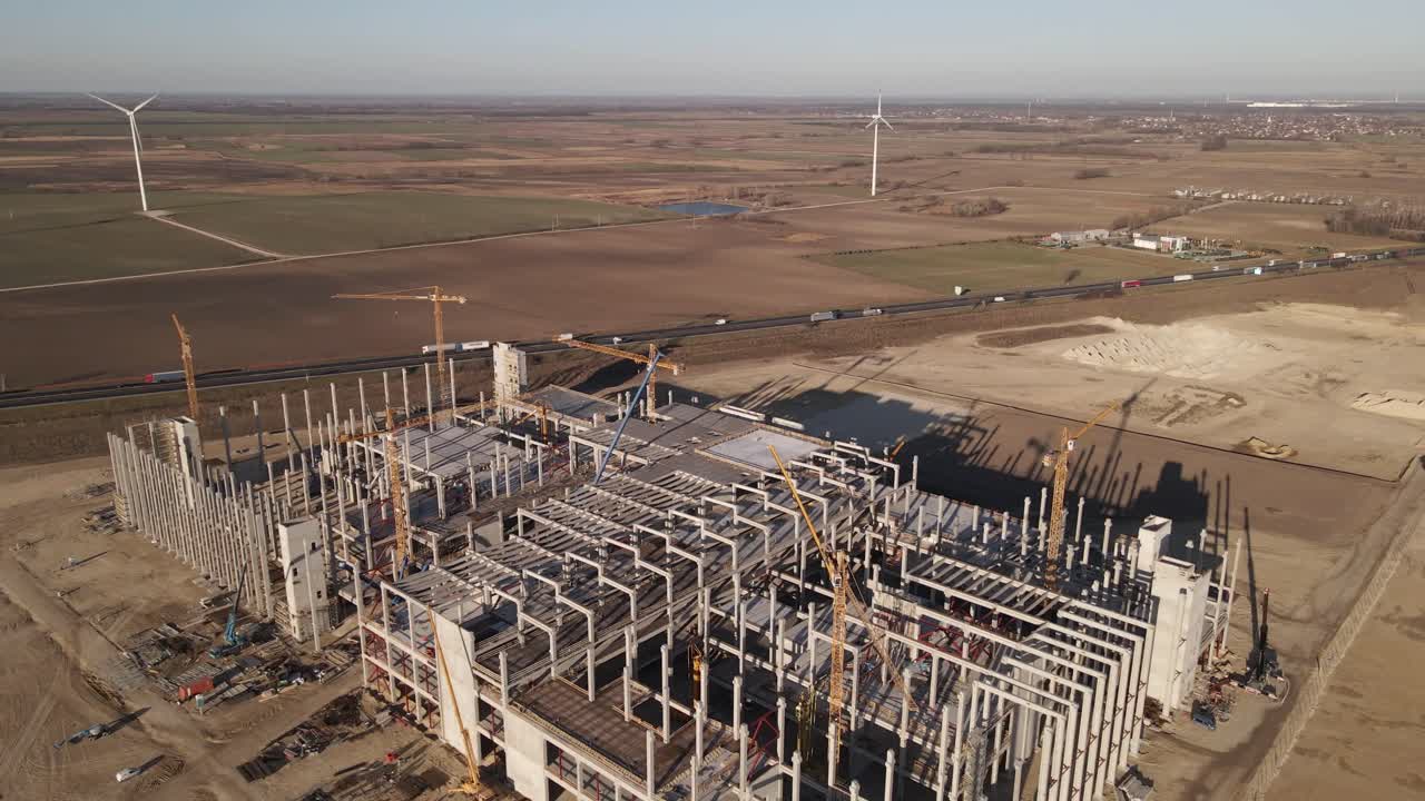 Aerial View of Large Industrial Construction Site. Drones flies over it, next to the highway with moving trucks and cars.