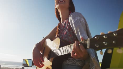 Happy-caucasian-woman-sitting-in-beach-buggy-by-the-sea-playing-guitar