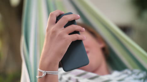 mujer relajándose en una hamaca y usando su teléfono