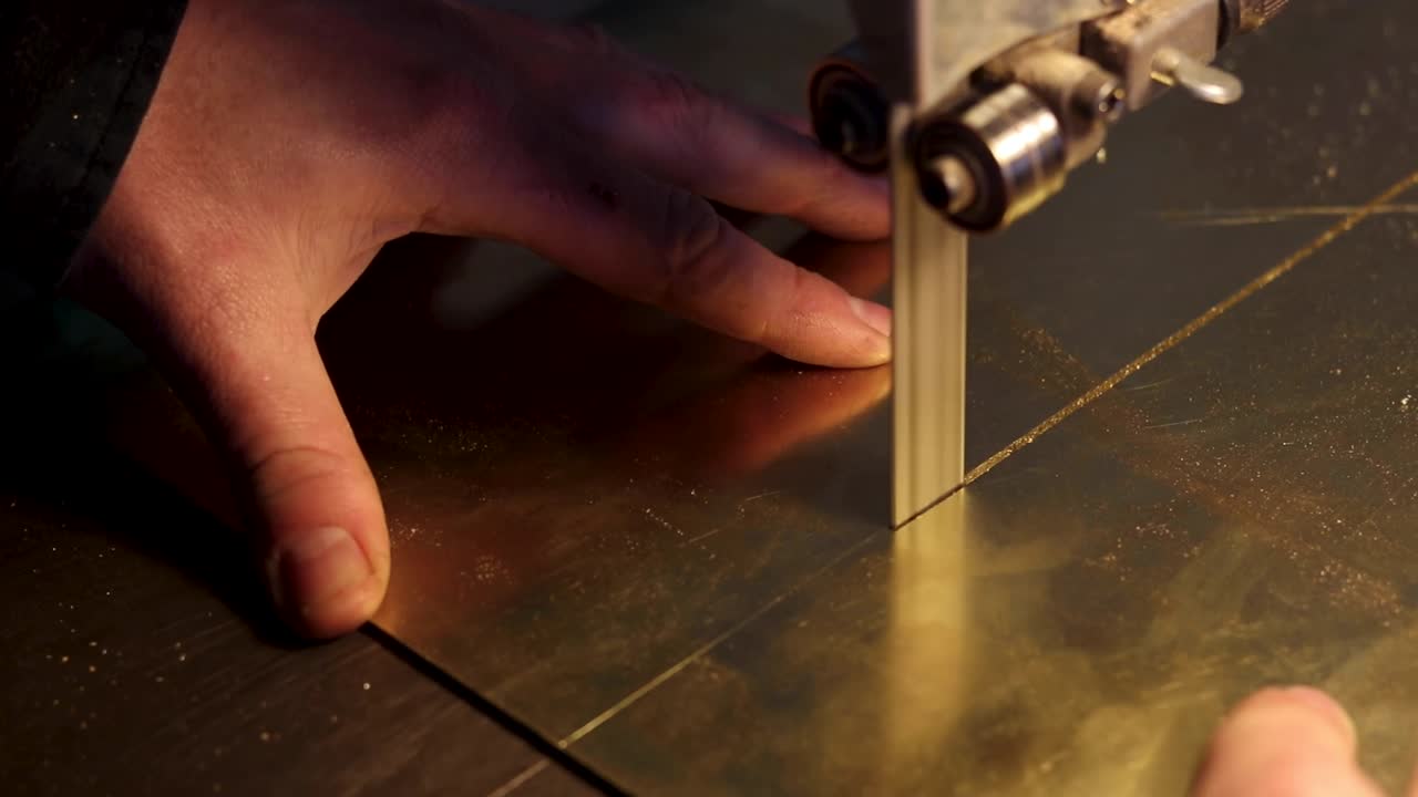 imágenes de primer plano del corte de metal de latón con una sierra de banda con la mano del hombre empujando una hoja de latón a través de la sierra