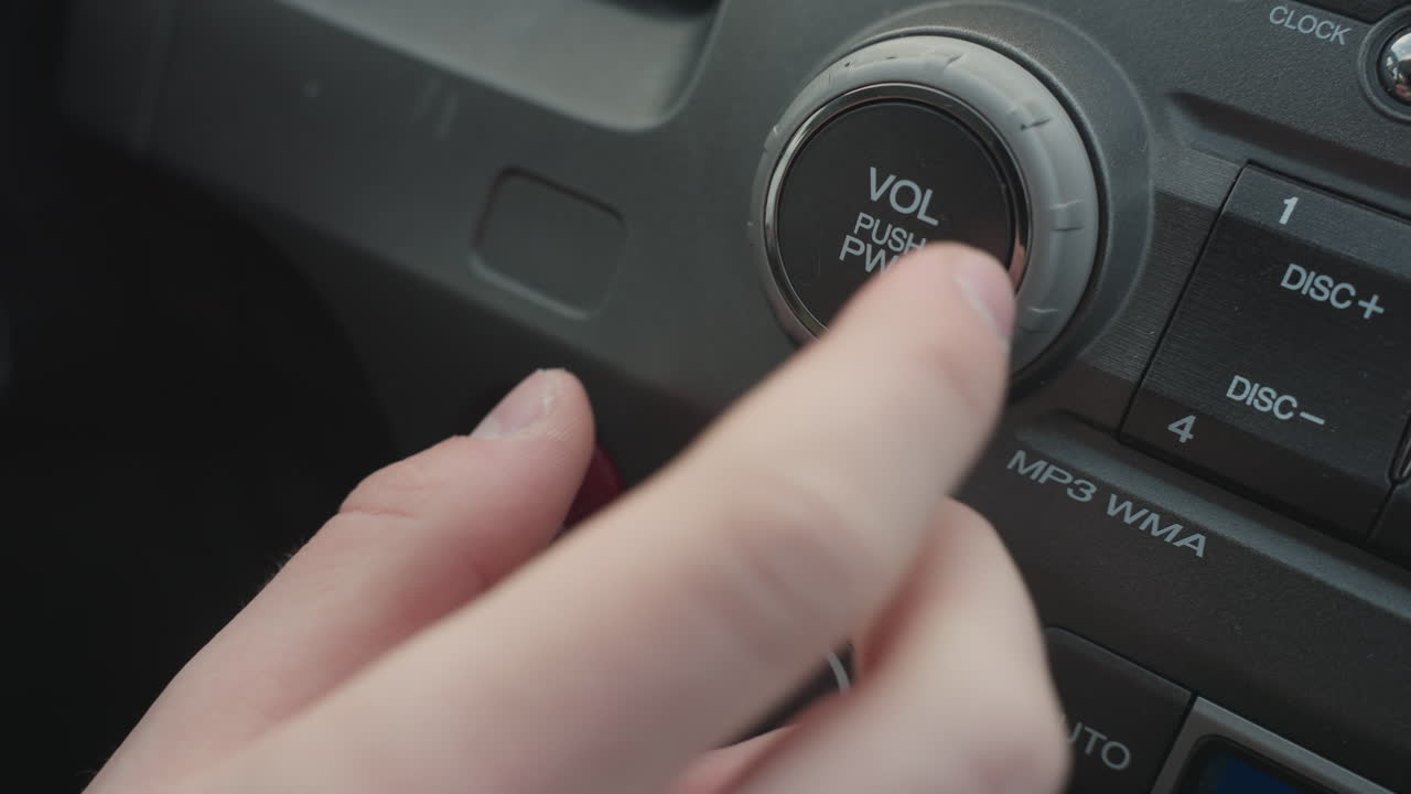 Close up of person turning audio volume knob and pressing push button on car dashboard control panel showing finger interaction with rotary dial and media power function in modern vehicle interior
