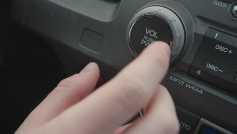close up of person turning audio volume knob and pressing push button on car dashboard control panel showing finger interaction with rotary dial and media power function in modern vehicle interior